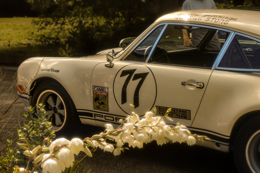 White number 11 Porsche race car surrounded by sunlit flowers, photographed by Jordan Lombard
